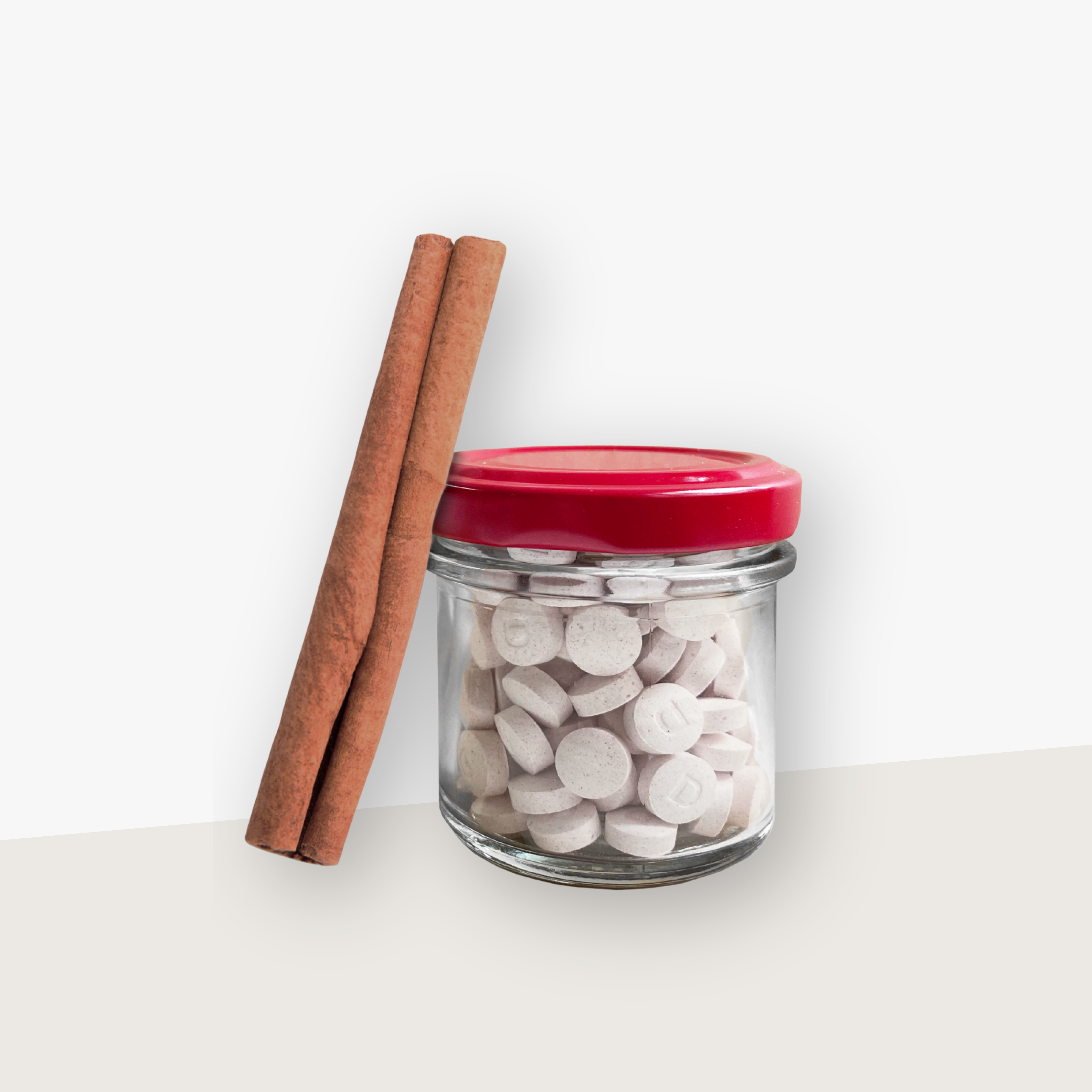 Ein Aufbewahrungsglas mit rotem Deckel gefüllt mit Denttabs in Zimtgeschmack. Eine Zimtstange lehnt an dem Glas. Der Hintergrund ist hell.
