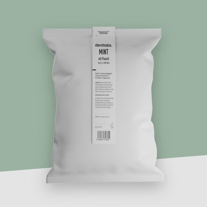 Ein weißer Beutel voll mit 1 Kilogramm Zahnputztabletten vor einem pastellgrünen Hintergrund.
